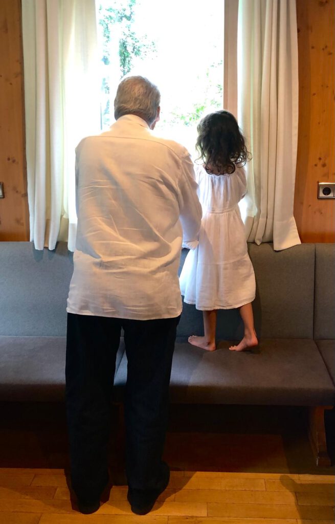 Ein Großvater und seine Enkelin schauen aus einem geschlossenen Raum in die helle Welt hinaus.