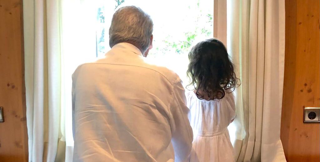 Ein Großvater und seine Enkelin schauen aus einem geschlossenen Raum in die helle Welt hinaus.
